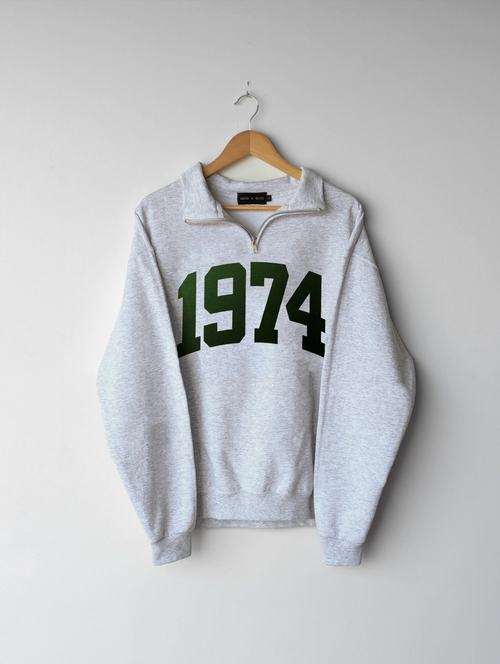 Gray quarter zip sweatshirt with '1974' printed on it, hanging on a wooden hanger against a white background. 1974, birthday, gift ideas