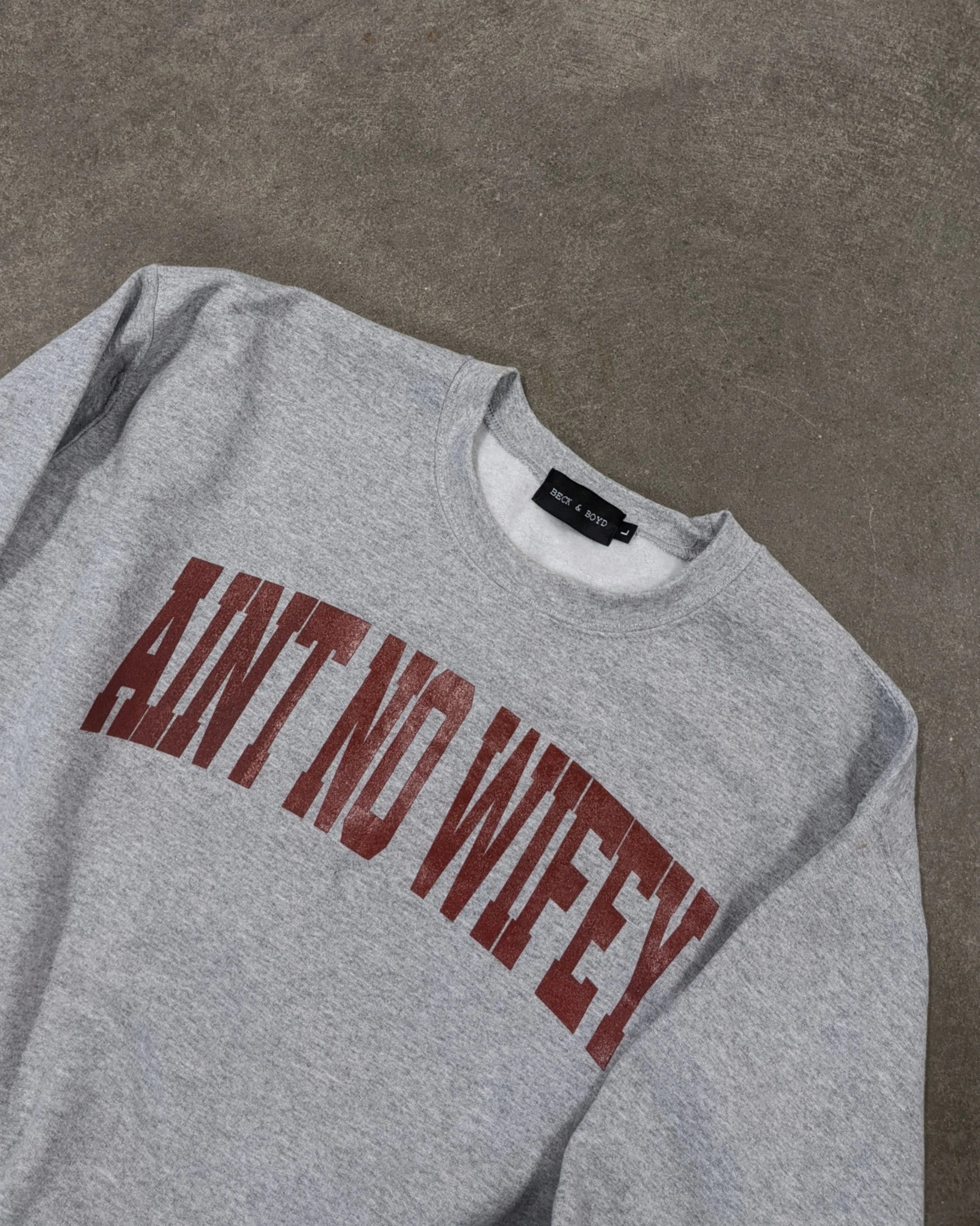 Grey sweatshirt with 'AINT NO WIFEY' text on a brown background, Wifey, single, Valentines day, aint no wifey, gift ideas, independent woman