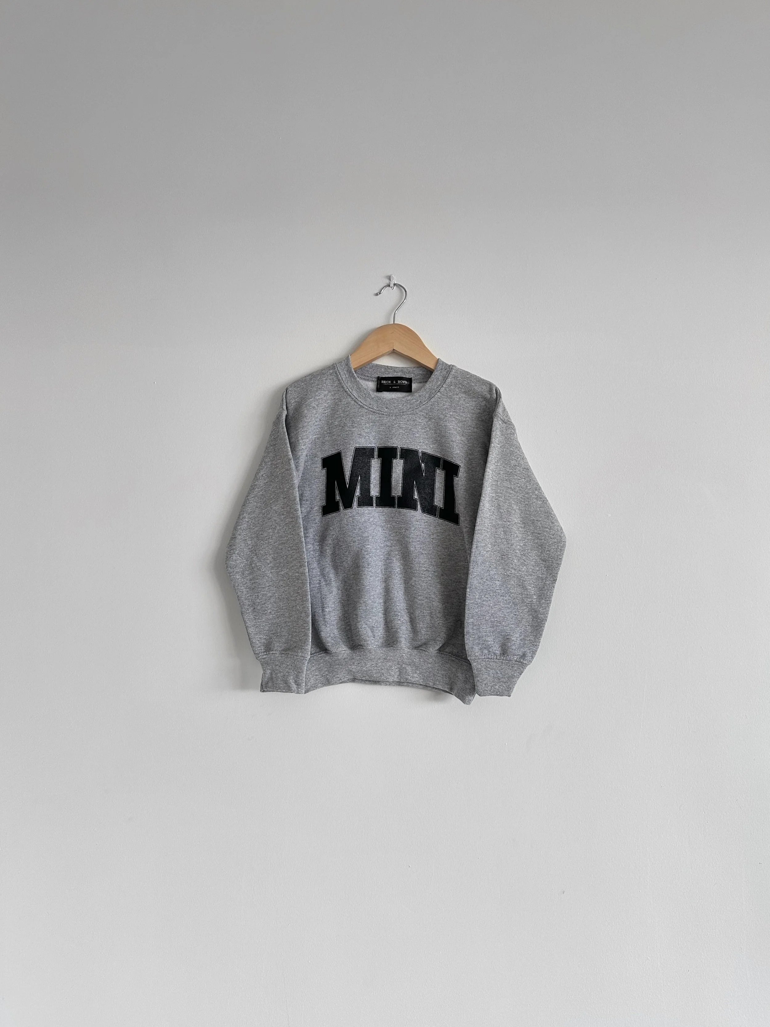 Grey kids sweatshirt with 'MINI' print on a hanger against a plain background, mini, matching sweaters, baby, toddler sweater, kids