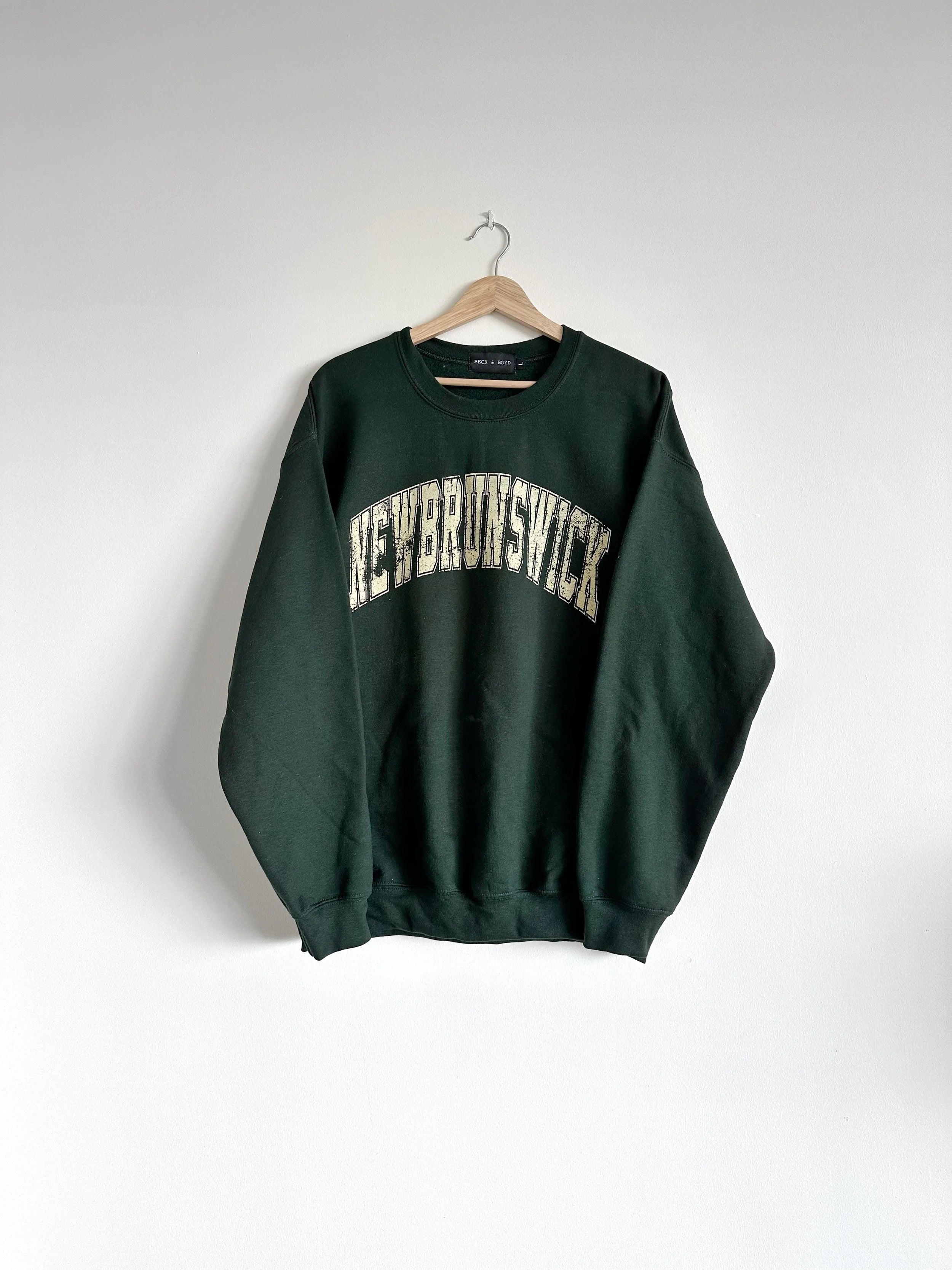 Green sweatshirt with 'New Brunswick' text on a hanger against a white background, NB, New Brunswick, Retro, Retro vibe, vintage, dads sweater, cozy