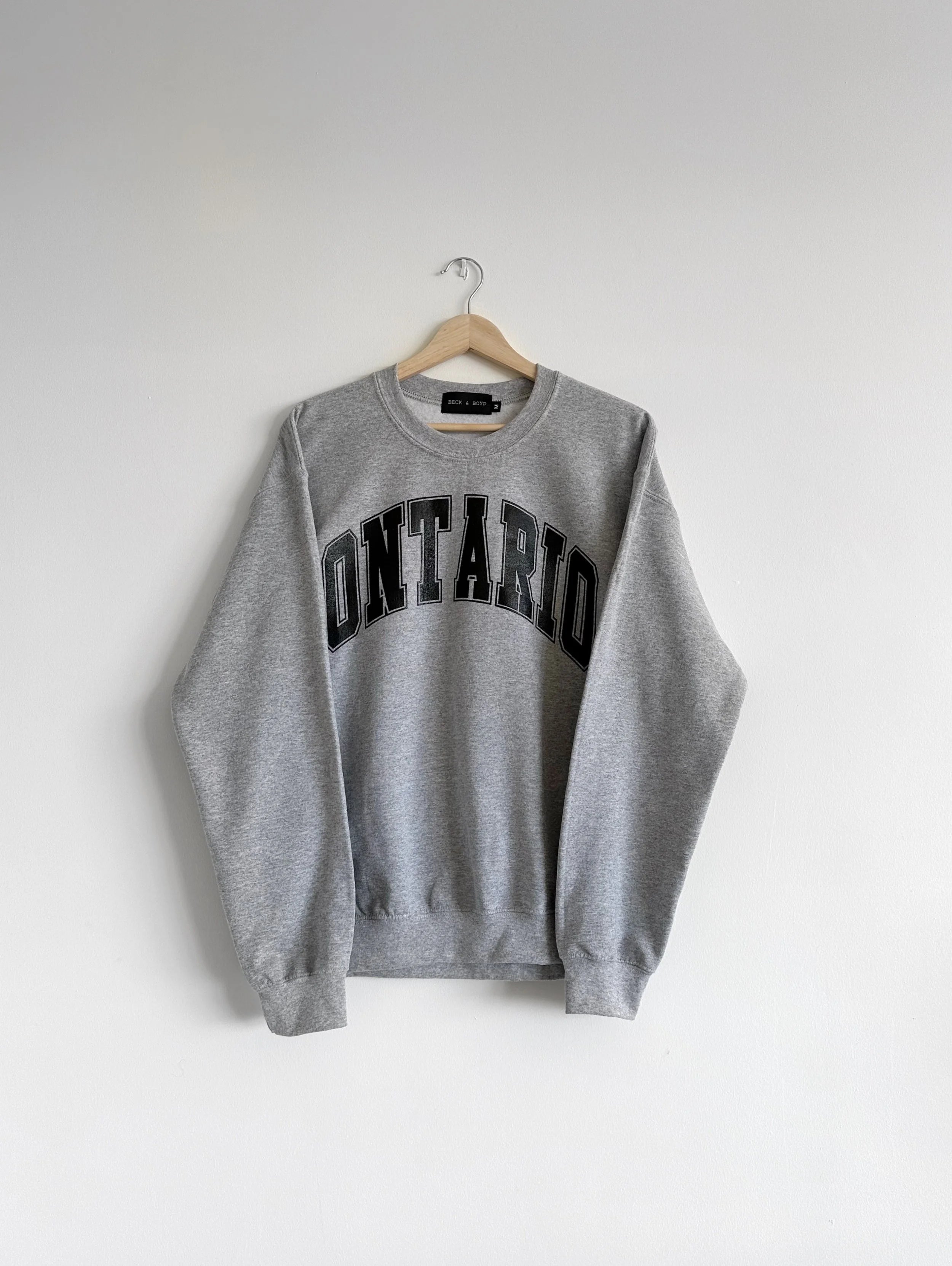 Grey sweatshirt with 'ONTARIO' text on a hanger against a white background, ontario, Canada, Cozy, gift ideas, Toronto