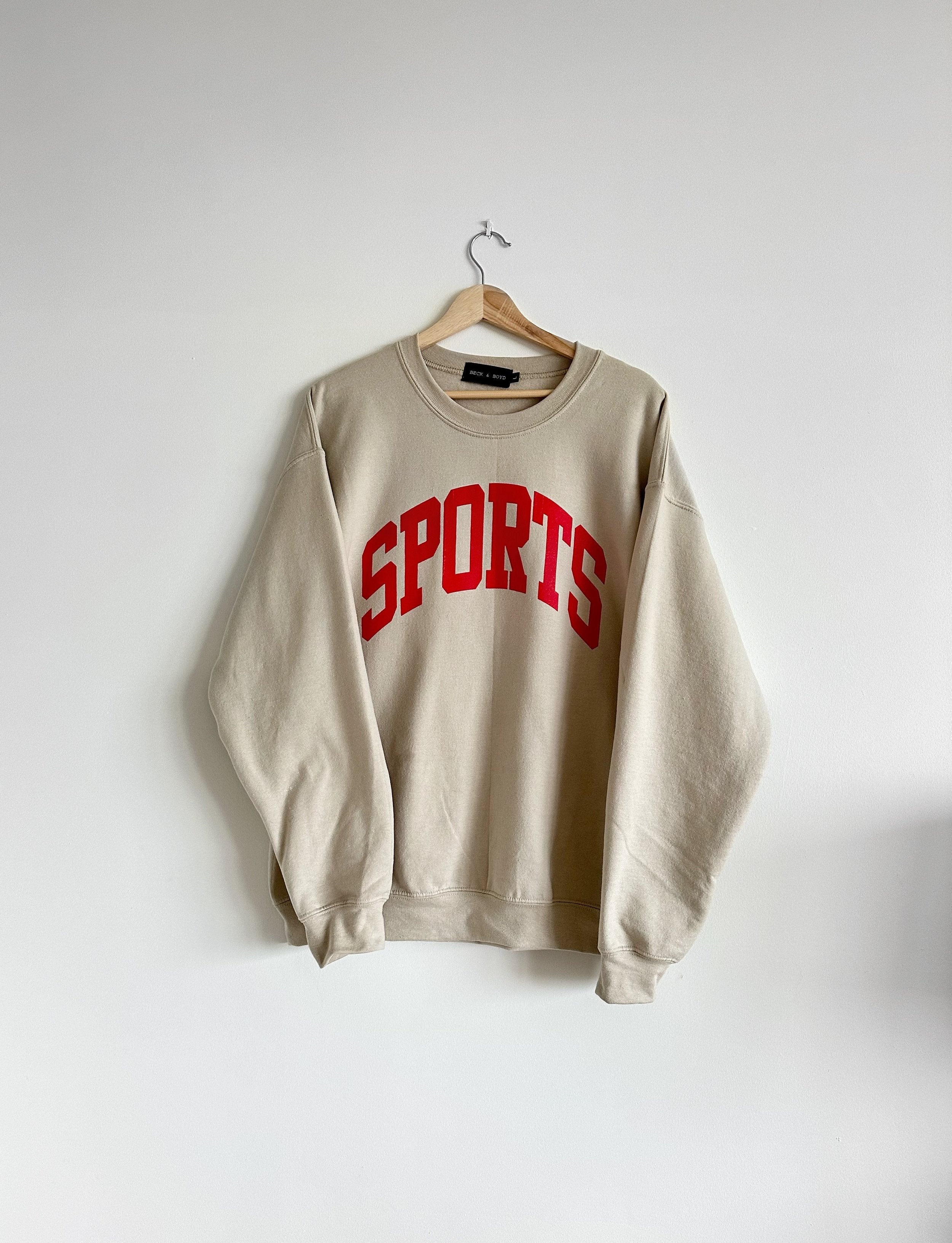 Beige sweatshirt with 'SPORTS' in red text on a white background, Taylor Swift, Travis Kelce, Kansas City Chiefs, Sporty Chic, Sports, Sports GF, Sport Girlfriend, Merch, TSwift, Swifties, Swiftie merch, Beige